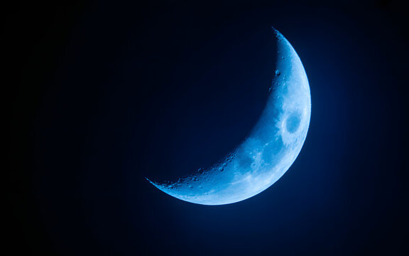 Close-up view of a vibrant blue crescent moon against a dark night sky