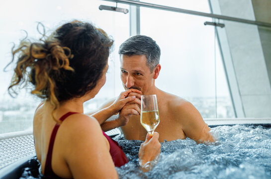Middle aged couple relaxing in hot tub at spa and drinking champagne.