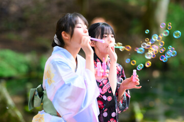 Obraz premium 浴衣を着た日本人の小学生の女の子がシャボン玉で遊ぶ夏の風景