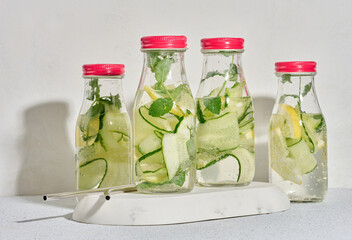 Glass bottles with red lids, filled with detox water containing cucumber and lemon slices and mint...
