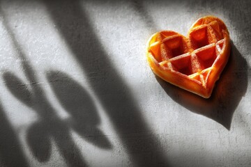 Heart shaped waffle with strong shadows on textured surface