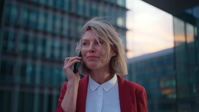 Professional businesswoman in red jacket confidently standing in front of modern glass skyscraper, embodying success and corporate leadership with radiant smile and executive presence