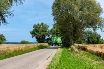 Green grain harvester riding on the wheat field. Summer harvest of the grain during sunny day.
