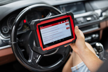 Modern technology in auto repair – mechanic using electronic car diagnostic tool. mechanic holds a modern diagnostic scanner inside a car, checking vehicle systems and electronics.