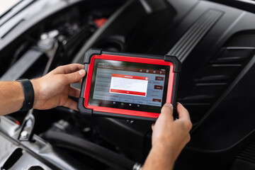 Close-up of a technician holding an advanced diagnostic device inside a car, performing system checks. Modern automobile maintenance and electronic diagnostics