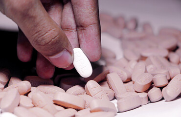 A Detailed Close-up of a Hand Delicately Selecting a White Pill from a Large, Scattered Pile of Beige and Pink Pharmaceutical Tablets