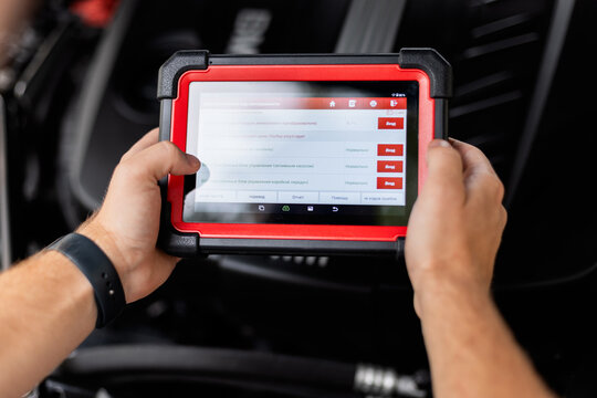 mechanic holds a modern diagnostic scanner inside a car, checking vehicle systems and electronics. Automotive technology and repair concept with professional diagnostic tool in use