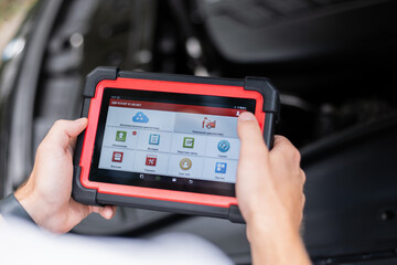Modern technology in auto repair – mechanic using electronic car diagnostic tool. Mechanic using a digital diagnostic scanner to check car systems inside the vehicle.
