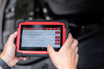 Mechanic using a digital diagnostic scanner to check car systems inside the vehicle. Modern technology in auto repair – mechanic using electronic car diagnostic tool.