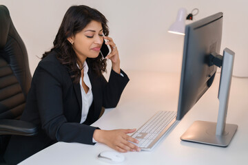 Businesswoman working at desk while talking on phone in modern office environment