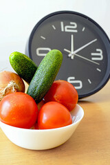 Tomatoes, cucumber and onion near the clock showing 12:10. Intermittent fasting schedule concept. Popular health trend combining fresh produce with timed eating patterns. Diet and wellness industry