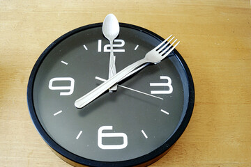Intermittent fasting concept: fork and spoon on clock face representing time-restricted eating...