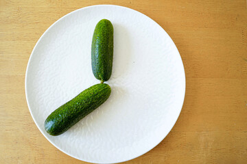 Minimalistic food photography: two fresh cucumbers on a white plate - a composition that reminds one of a clock face with hands. Clean eating and whole foods concept. Low-calorie vegetable snack. 
