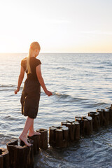 Cute adorable blond teenager happy kid girl walking by wooden breakwater posts at Baltic sea scenic...