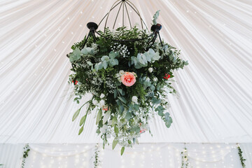 Hanging floral chandelier with roses, eucalyptus and greenery decoration under white draped wedding tent with romantic lights