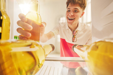 Young man taking cold beer bottle from fridge view with excitement. Concept of advertising...