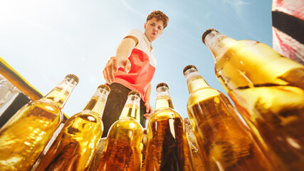 Young man choosing beer bottle from outdoor cooler under summer sky, low angle. Concept of alcohol...