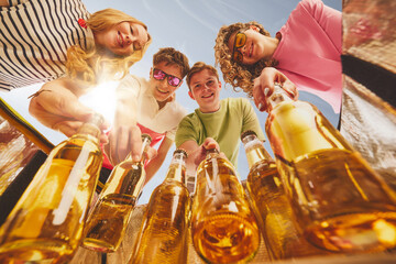 Friends smiling and picking cold beer bottles from cooler under sunlight, low angle. Concept of...