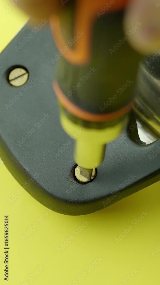 Poster vertical macro view of a screwdriver bit tightening a brass screw into a black metal plate against a