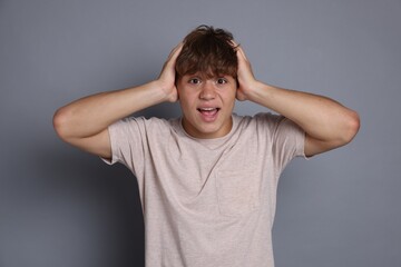 Teenage boy suffering from panic attack on grey background
