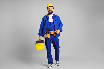 Professional repairman with tool box on grey background