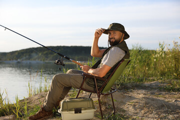 Fisherman with rod sitting on chair and fishing near lake at summer