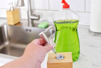 A bottle with detergent and a bottle with a dispenser for daily use of detergent in the kitchen near the sink. Poured from a large container into a convenient one.