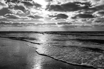 Black-and-white panorama on the beach of the North Sea island of Norderney (Germany) at low sun with roaring surf in the Wadden Sea National Park. High-contrast seascape and vacation destination.