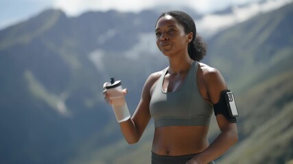 Young woman in sportswear enjoying refreshing water from a bottle, surrounded by a breathtaking mountain landscape after completing an invigorating workout, embodies a healthy lifestyle