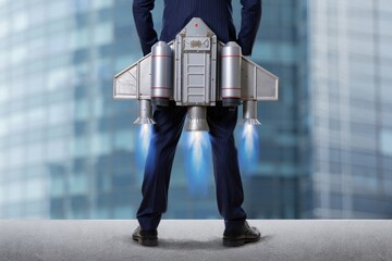 Obraz na płótnie Canvas Rear view of man in suit with jetpack standing on rooftop with city building background