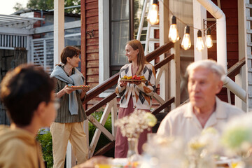 Two Caucasian women, one teenager and one middle aged, standing outdoors holding plates of food and...