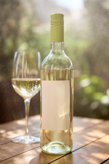White wine bottle with blank label and glass on wooden table, mockup for ad, text. Concept of alcohol branding, menu design, lifestyle content, event promotion and social media storytelling.
