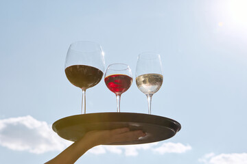 Red white and rose wine glasses on tray against blue sky. Concept of alcohol tourism, event promotion, festivals, lifestyle visuals, social media and modern hospitality branding.