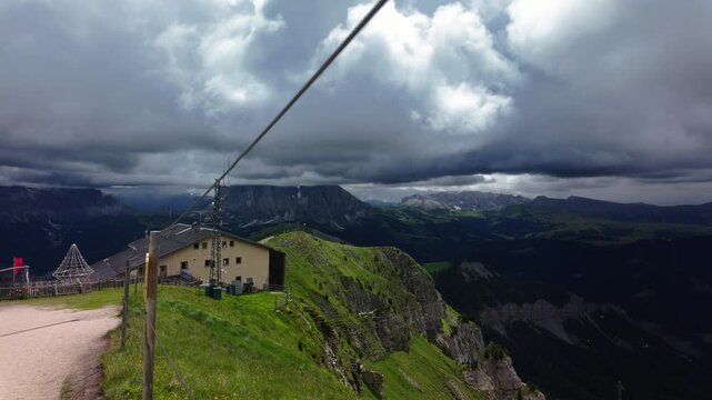 Scenic view from Seceda peak in the Dolomites with dramatic clouds, green cliffs, mountain hut, and flock of birds soaring over the ridge, Northern Italy