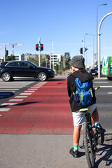 Young teen cyclist standing on crosswalk with bicycle, stopping at red traffic light as cars pass,...