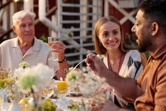 Caucasian senior man, Caucasian young adult woman, and Middle Eastern young adult man sitting outdoors sharing meal and conversation at table decorated with flowers and candles
