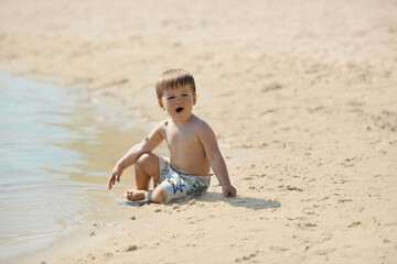 Little boy in shorts playing on wet sandy beach. Concept of childhood fun, vacation, outdoor leisure, summer mood, innocence, carefree lifestyle and recreation.