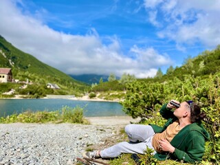Tourist relaxing by alpine lake Zelené pleso, observing mountains with binoculars. Concept: outdoor exploration, slow travel, sustainable lifestyle.
