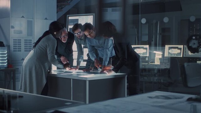 Several Indivis Gather at a Central Table, Reviewing Printed Schematics and Digital Displays. the Group Discusses Technical Data, Referencing Diagrams and Computer Screens to Support Analysis