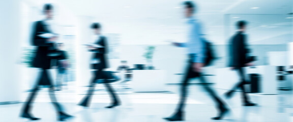 Obraz premium Blurred people walking in a bright office environment filled with natural light, glass walls, and open layouts that highlight motion, collaboration, and a contemporary workplace atmosphere.