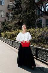 A Fashionable Woman in a Flowing Black Skirt and White Blouse Stands Elegantly Alongside a Sunlit...