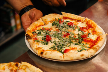 Authentic kitchen atmosphere with chef serving freshly baked pizza topped with arugula and cherry...