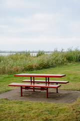 Obraz premium Red metal picnic table stands ready on a concrete slab, with a picturesque natural backdrop.