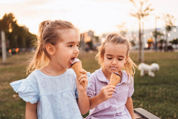 Fototapeta premium Two little girls enjoying ice cream cones in a park at sunset