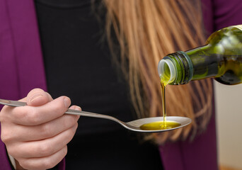 Woman pouring extra virgin olive oil onto a spoon, healthy fatty acids