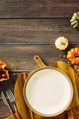 Autumn table setting with empty plate, vintage knife and fork, pumpkins, acorns, and dry flowers. Perfect for fall celebrations, Thanksgiving dinner concept
