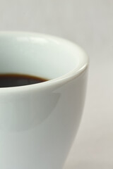 Elegant macro detail of a black coffee in a modern white ceramic cup. Minimalist morning concept with a clean bright background and excellent copy space for text.