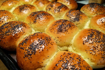 Freshly baked soft rolls topped with poppy seeds arranged on a baking tray in a cozy kitchen...