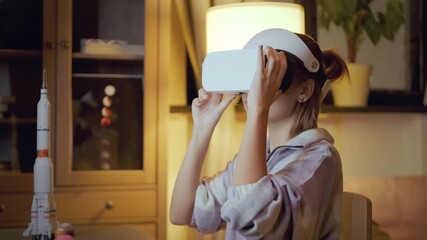 Modern Caucasian girl sitting at desk in living room typing something on laptop then turning on VR headset - Powered by Adobe