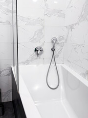 Bathtub with mixer and shower. White marbble tiles. Modern bathroom interior.